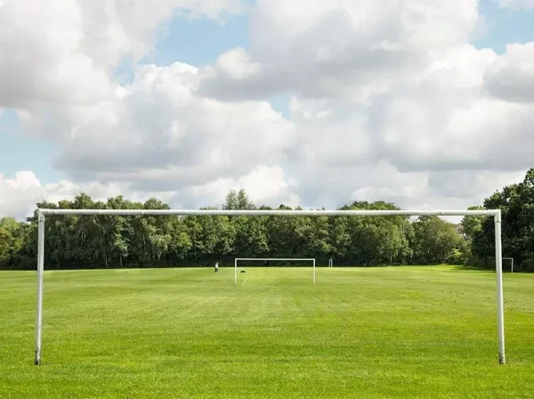 Football pitch with goalposts. Green grass pitch and blue sky with clouds.